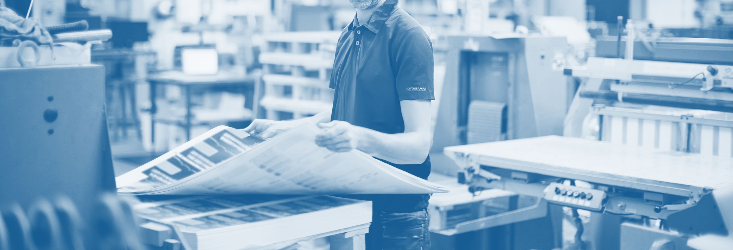 Tecnico tipografico che esamina grande foglio stampato in officina servizi stampa digitale e offset. Sprint24.