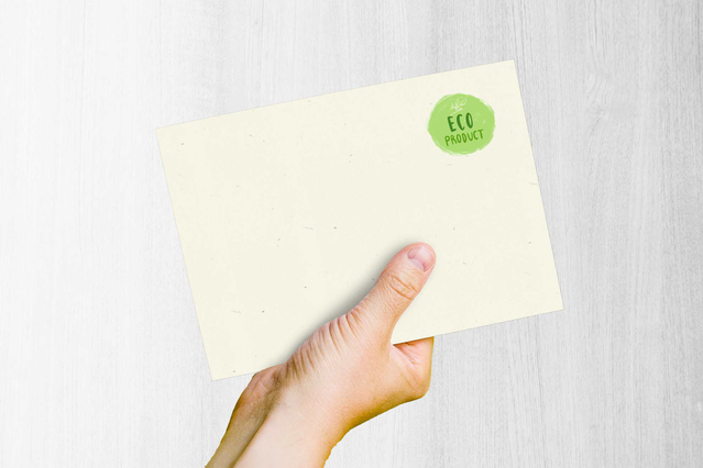 Mano che regge una busta Woodstock Betulla naturale con etichetta eco Mano con busta Woodstock Betulla naturale con etichetta eco verde. Carta fibre riciclate Sprint24.